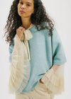 Woman wearing a light blue poncho with beige accents on a white background