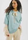 Woman wearing a light blue sweater with a beige bow tie and beige pants on a white background