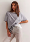 Woman wearing a gray t-shirt and light-colored pants against a plain background