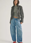 Person wearing a black leather jacket, striped shirt, and blue jeans on a white background