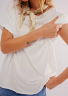 Person wearing a white top and blue jeans with a decorative scarf around their neck.