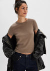 Woman wearing a brown t-shirt and dark jeans with a black jacket on a white background