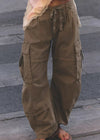 A person wearing loose, wide-leg cargo pants in an olive-brown/khaki color, standing barefoot on gray pavement.