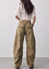 A model shown from the back wearing wide-leg olive cargo pants and a white textured short-sleeve crop top against a plain light gray studio background.