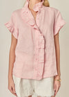 Woman wearing a pink ruffled blouse and white shorts on a beige background
