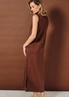 A woman modeling a sleeveless, high-neck, midi-length brown knit dress with a side slit, posed against a solid brown studio backdrop.