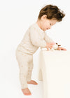 Child in a cream-colored outfit playing with a toy on a white surface