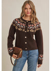 A woman modeling a dark brown button-up knit cardigan with a colorful Fair Isle pattern across the yoke and cuffs, paired with blue jeans and holding a brown leather crossbody bag against a solid beige background.
