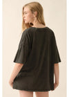 A woman wearing an oversized dark olive green short-sleeve t-shirt, shown from the back against a plain beige studio background.
