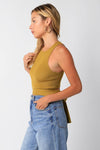 Woman wearing a mustard yellow ribbed tank top and blue jeans on a white background