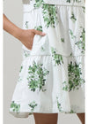 White dress with green leaf pattern worn by a person on a plain background