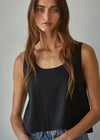A woman wearing a black sleeveless scoop-neck top and blue jeans, photographed against a plain light gray studio background.
