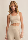 Woman wearing a beige ribbed tank top and pants against a neutral background