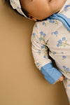 Child wearing a floral onesie with blue cuffs against a beige background