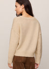 Woman wearing a beige sweater and brown pants against a plain background