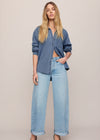 Woman wearing a denim shirt and light blue jeans against a beige background