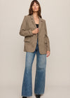 Woman wearing a patterned blazer and blue jeans on a plain background