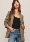 Woman wearing a brown checkered blazer, black top, and blue jeans on a beige background