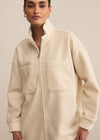 Woman wearing a beige zip-up jacket against a plain background