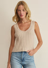 Woman wearing a beige ribbed tank top and blue jeans against a plain background