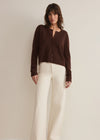 Woman wearing a brown cardigan and white pants against a plain background