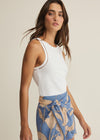 Woman wearing a white sleeveless top and blue floral skirt on a beige background