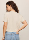 Woman wearing a beige sweater and blue jeans against a plain background